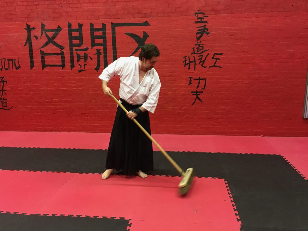 Image of an aikidoka sweeping the mats at the start of class so the session can start on time